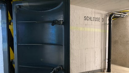Zu sehen ist eine große Schleusentür in einem Bunker, die geöffnet ist. Rechts auf der Wand steht "Schleuse 3".