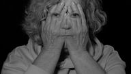 Schwarzweiß Aufnahme: Frau hält sich beide Hände vor ihr Gesicht, auf den Handrücken sind ihre Augen, ihre Nase und ihr Mund zu sehen (Fotobearbeitung)