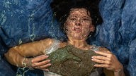 Eine Frau mit einem großen Stein auf der Brust liegt unter Wasser