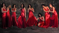 Acht Frauen in einem roten Satinkleid stehen in einer Reihe vor einem schwarzen Hintergrund 