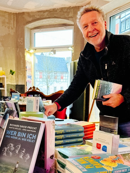 Ein lachender Mann hinter einem Büchertisch