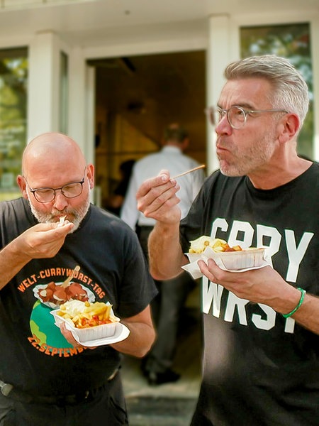 Zwei Männer essen eine Currywurst