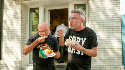 Zwei Männer essen eine Currywurst