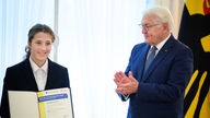 Links steht ein junges Mädchen mit einer aufgeschlagenen Urkunde in den Händen, rechts von ihr klatscht Bundespräsident Frank-Walter Steinmeier