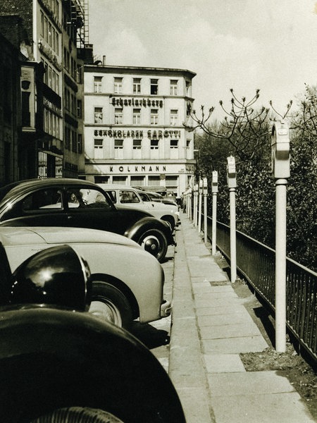 Parkuhren stehen vor geparkten Autos an einer Straße in Duisburg.