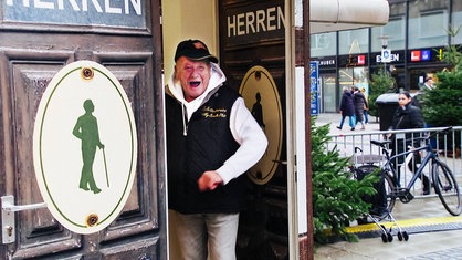 Alfred Blömecke steht in der Tür der Herrentoilette und singt.