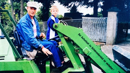 John Reinarz als Kind auf einem Fahrzeug am Friedhof.