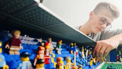 Jonas stellt die Lego-Figuren auf die Tribüne seines Lego-Stadions.