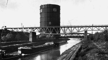 Ein schwarz-weiß Foto eines Gebäudes in "Tonnenform" an einem Fluss