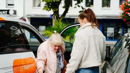 Eine junge Frau hilft einer Seniorin beim Aussteigen aus einem Auto