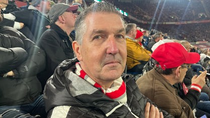 Ein Mann sitzt im Stadion, er trägt einen rot-weißen Schal von Fortuna Düsseldorf.
