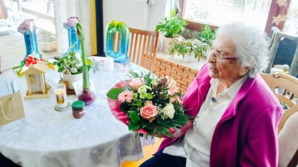 Die 110-jährige Elisabeth Rüterbories sitzt mit Blumen in der Hand vor einem gedeckten Tisch