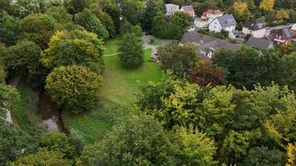 Luftaufnahme: Blick auf grüne Wiesen und Bäume, einen Fluss und Häuser