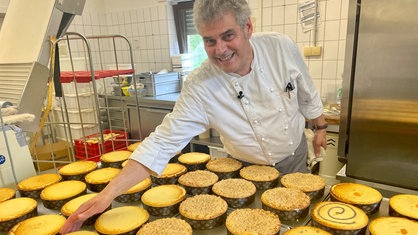 Mann im weißen Bäckerkittel schöpft die Kuchenfüllung aus einem großen Topf in die Käsekuchenform.