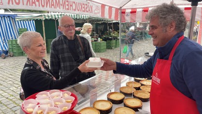 Eine Frau und ein Mann nehmen eine Schachtel an einem Marktstand entegegen.