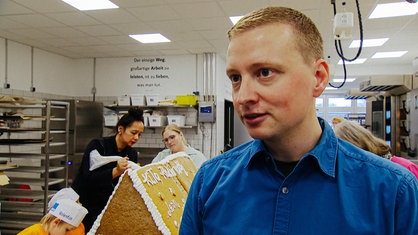 Erik Staschöfsky im Portrait, im Hintergrund wird gerade ein großes Lebkuchenhaus dekoriert.