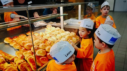 Mehrere Kinder staunen über frisches Gebäck in der Auslage der Backstube