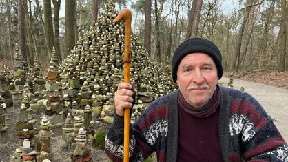 Künstler Markus Gern kniet im Steinmännchen-Wald in Kleve vor einem hohen Hügel aus Steinen
