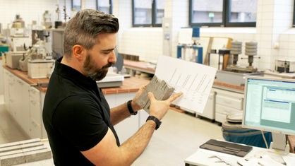 Daniel Wulff-Janssen von der TH Köln steht im Labor. In der einen Hand hält er einen Zettel mit den Prüfergebnissen, in der anderen eine Steinprobe.