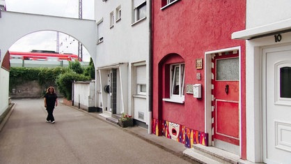 Ein Haus in einer Straße ist rot gestrichen, am Sockel ist ein buntes Motiv gemalt.