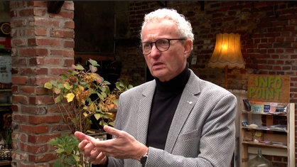 Ein Mann mit grauen Haaren und Brille steht im Innenhof des Bauernhofs.