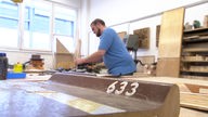 In der Werkstatt der Neuen Arbeit der Diakonie Essen liegt eine alte Holzsitzbank aus der Lohrheide, ein Schreiner schleift de Bänke ab.