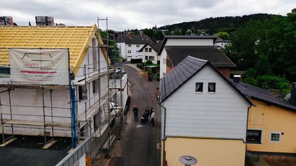 Eine Straße mit mehreren Häusern aus der Vogelperspektive. Das Haus auf der linken Seite ist in einem Baugerüst.