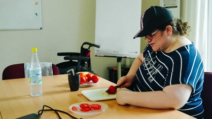 Eine Frau mit blau-weiß gestreiften Shirt und Kappe beim Tomaten schneiden