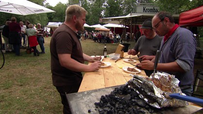 Hobbyköhler Christof Kordes und zwei weitere Männer essen den Erdlochbraten aus dem Kohlemeiler