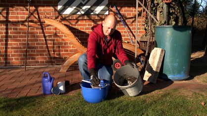 Jürgen Korff wäscht das Material aus der Dachrinne mit einem Küchensieb und einem Eimer Wasser