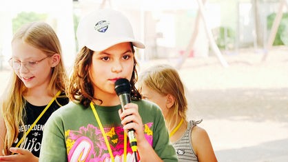 Bruna bei ihrer Wahlrede in Mini-Siegburg. Sie hält ein Mikrofon vor ihren Mund.