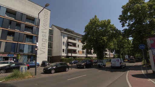 Die Ostheimer Straße in Köln-Vingst mit parkenden Autos und dem Schriftzug "Vingst Veedel" auf einem Haus