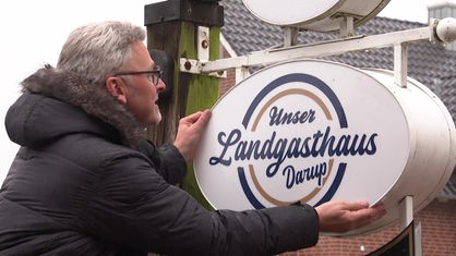 Ein Mann hängt ein neues Leuchtschild mit der Aufschrift "Unser Landgasthaus Darup" auf.
