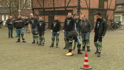 Eine Mannschaft beim Oster-Hasseln in Dülmen-Buldern, die Spieler haben Teppichreste an den Schienbeinen, einer hebt die Holzscheibe Hassel auf.
