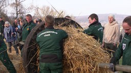 Mitglieder des Osterdechenvereins Lügde stopfen Stroh in ein großes Holzrad