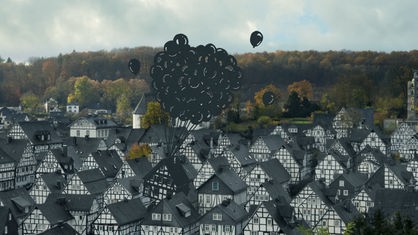 Ausschnitt aus der WDR-Kampagne des Scherenschnitt-Künstlers Paperboyo: In Freudenberg wird ein Fachwerkhaus von Luftballons nach oben gezogen