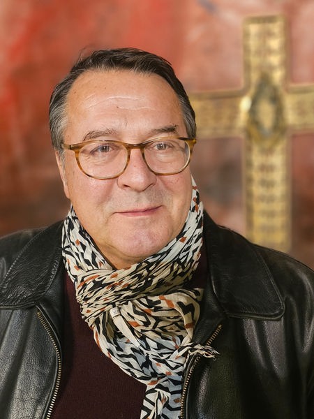 Pfarrer Hans Mörtter steht vor einem Kreuz und lächelt leicht in die Kamera