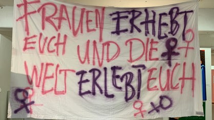 Ein Banner mit der Aufschrift "Frauen erhebt euch und die Welt erlebt euch"