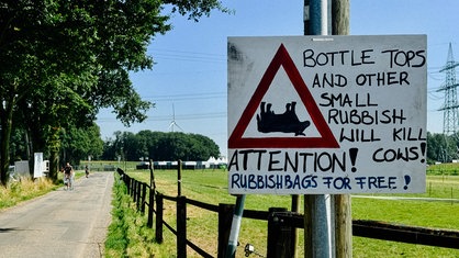 Zu sehen ist ein selbstgemaltes Schild am Wegesrand, auf dem dazu aufgerufen wird, keinen Müll liegen zu lassen.