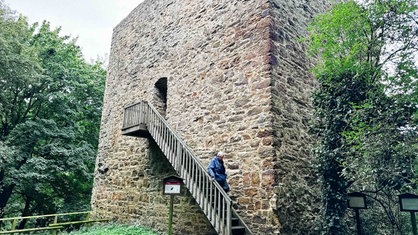 Ein mittelalterlicher Turm mit einer Holztreppe. Ein Mann steigt die Treppe hinab.