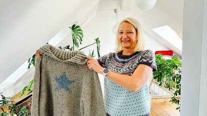 Eine Frau hält einen selbstgestrickten Pullover hoch.