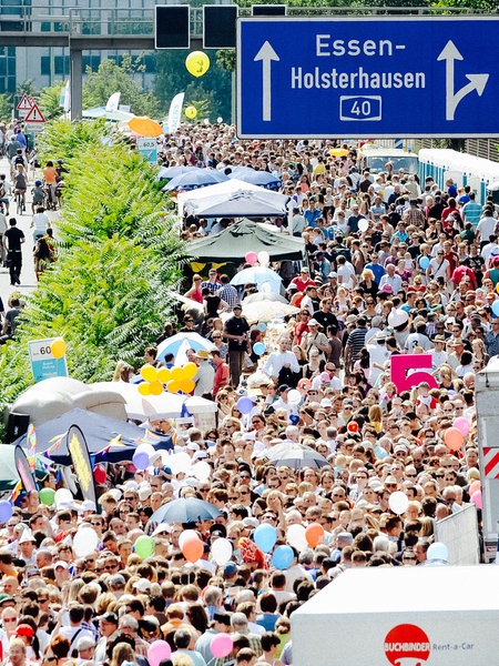 Zahlreiche Menschen tummeln sich zwischen Pavillons auf der A40 bei Essen. In der gegenüberliegenden Fahrtrichtung sind Radfahrer unterwegs.