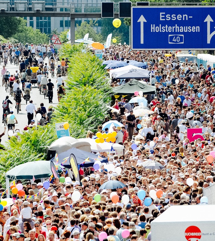 Zahlreiche Menschen tummeln sich zwischen Pavillons auf der A40 bei Essen. In der gegenüberliegenden Fahrtrichtung sind Radfahrer unterwegs.