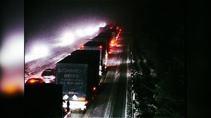 Auto und Lkws stehen auf einer Autobahn im Schnee im Stau.