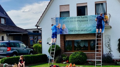 Zwei Manner befestigen ein Transparent an einem Balkon.