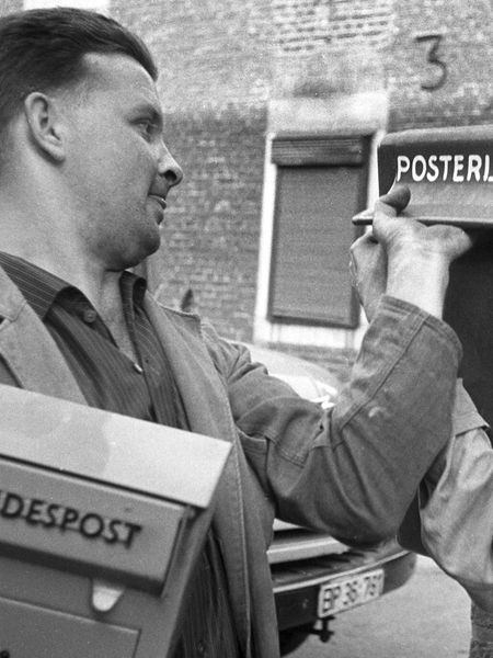 Zwei Männer tauschen einen niederländischen Briefkasten an einer Wand gegen einen deutschen aus.