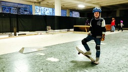 Ein Mädchen mit Skateboard, Knie- und Armschonern und Helm in einer Halle