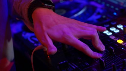 Zu sehen ist eine Hand, die ein DJ-Pult betätigt.
