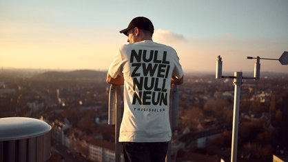 Ein Mann trägt ein T-Shirt mit der Aufschrift "Null Zwei Null Neun This Is Gelsen" auf dem Rücken