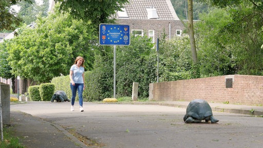 Eine Frau läuft über eine Brücke auf der zwei lebensgroße Riesenschildkröten aus Metall stehen